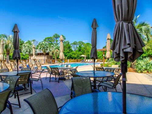 un patio al aire libre con mesas y sombrillas y una piscina en Redfish Village M2 423, en Blue Mountain Beach