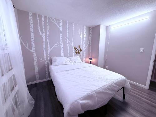 a bedroom with a bed with white sheets and trees on the wall at 4 Bedroom House steps to 401, Perfect for long stays in Belleville