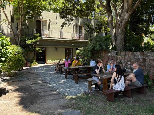 a group of people sitting at picnic tables under a tree at Viajero Colonia Hostel in Colonia del Sacramento