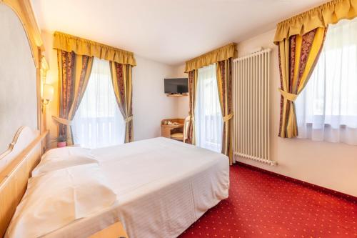 a bedroom with a white bed and two windows at Hotel Plank in San Martino di Castrozza