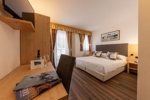 a bedroom with a bed and a desk and a television at Hotel Plank in San Martino di Castrozza