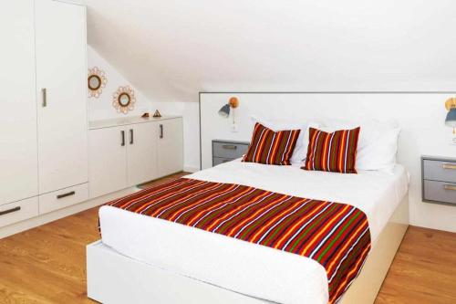 a white bedroom with a bed with red and orange pillows at SUNSCAPE STUDIO - Apt 1 Quarto, Ponta do Sol in Ponta do Sol