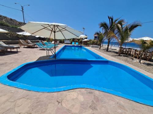 a blue swimming pool with an umbrella and the beach at Casuarinas Del Mar Chalet de 2 habitaciones in Canoas De Punta Sal
