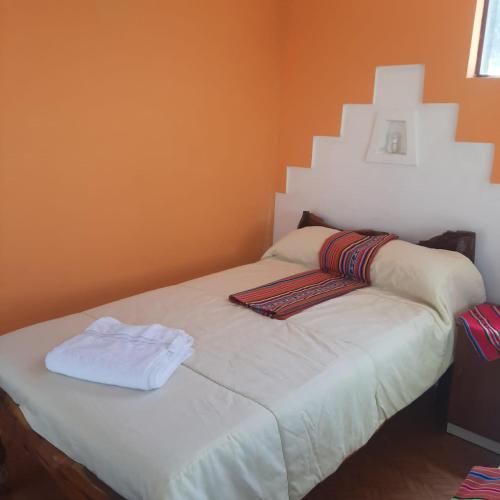 a bed in a room with an orange wall at Hostal Margarita in Comunidad Challapampa