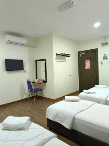 a room with three beds and a chair and a television at Hotel Bestari in Melaka