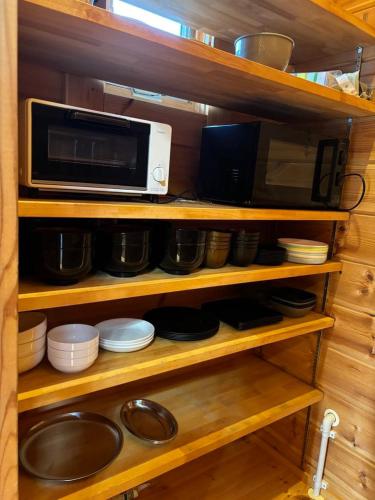 a kitchen shelf with a microwave and bowls and plates at SAUNA Log Cabin オーガスタハウス君津 in Kimitsu