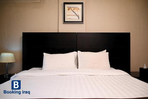 a bed with a black headboard and white sheets and pillows at Andalus Hotel in Baghdad