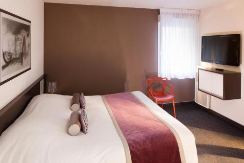 a bedroom with a bed with a television and a red chair at Hotel Le Bugatti in Molsheim