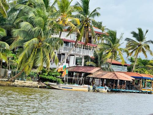 a building with palm trees and a boat in the water at Luthmin River View Hotel in Alutgama