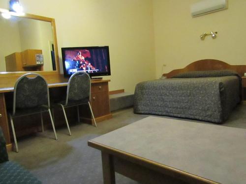 a room with a bed and a desk with a television at Glenelg Motel in Adelaide