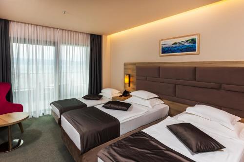 a hotel room with three beds and a red chair at Hotel Plaža Duće in Duće