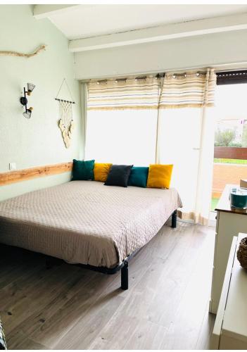 Cette chambre dispose d'un lit avec des oreillers colorés et d'une fenêtre. dans l'établissement L Aphrodite Studio Village Naturiste, à Port-Leucate