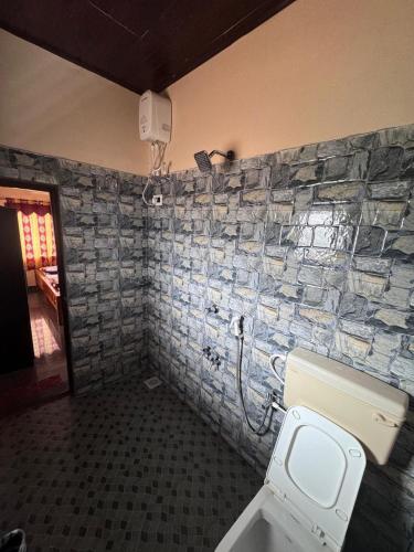 a bathroom with a toilet and a stone wall at Aikya homestay in Gokarna