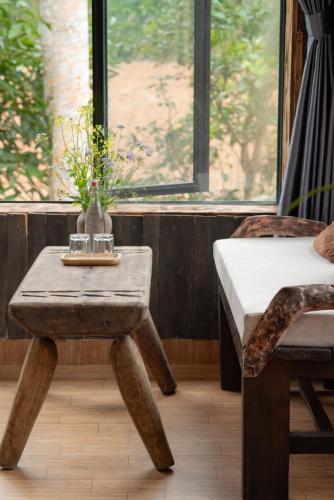 a table with a vase with flowers on it next to a window at Ha Giang Xanh Retreat - Trekking, Tour, Motorbike Rental in Ha Giang