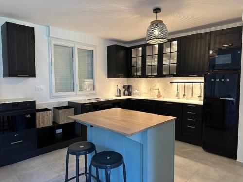 une cuisine avec des placards noirs et un îlot bleu avec des tabourets dans l'établissement La Brise Marine, à Barneville-Carteret