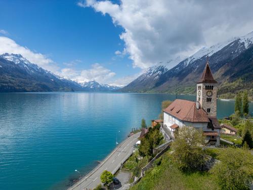a church on the shore of a lake with mountains at StayBrienz - Lake Brienz Family Holiday Apartment in Brienz