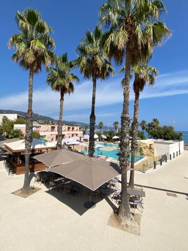 a pool with palm trees and a large umbrella at Résidence Kaliopé in Le Lavandou