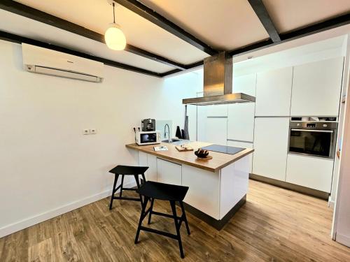 une cuisine avec des placards blancs et un comptoir avec deux tabourets dans l'établissement la fabrik - coeur de ville - clim, à Nîmes