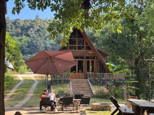 two people sitting under an umbrella in front of a cabin at Ban Kaew Mo Ra Glamping & Restaurant in Pang Mapha