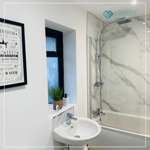 Un baño blanco con lavabo y ducha. en Tastefully decorated 4 Bed Home in Gedling - Near Colwick Country Park, Victoria Retail Park, City Centre & Nottingham Racecourse, en Nottingham