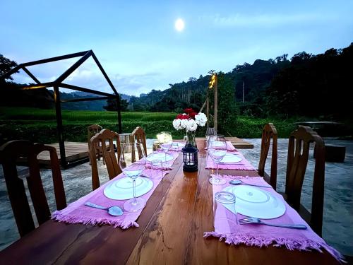 a long wooden table with plates and wine glasses at Ban Kaew Mo Ra Glamping & Restaurant in Pang Mapha