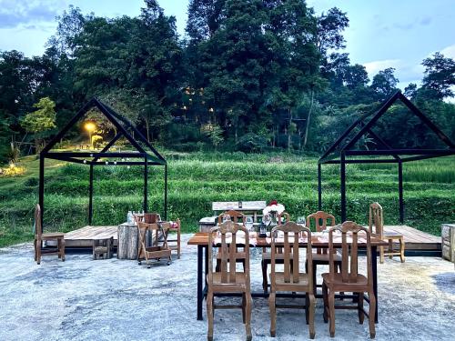 a wooden table and chairs in a field at Ban Kaew Mo Ra Glamping & Restaurant in Pang Mapha