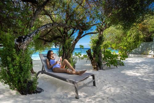 a woman sitting on a bench under a tree on the beach at OBLU NATURE Helengeli-All-Inclusive with free Transfers in North Male Atoll
