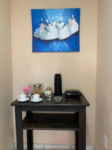 a table in a room with a painting on the wall at Suítes Benfica in Arraial d'Ajuda