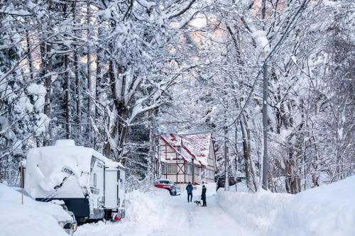 a snow covered street with a house and people walking in the snow at TERUKA白いテラスHakuba in Hakuba