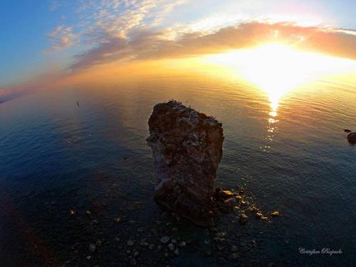 a rock in the middle of the water with the sunset at Hotel Piccolo Mondo in Acquappesa