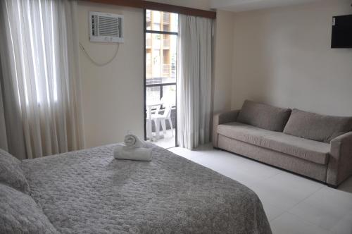a bedroom with a bed and a couch and a window at Champagnat Praia Hotel in Vila Velha