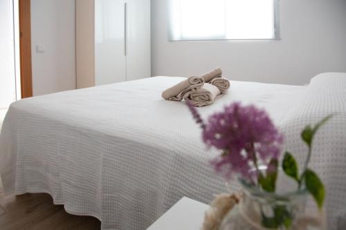 a white bed with towels and a vase of purple flowers at Jamaica Beach House in Puebla de Farnals