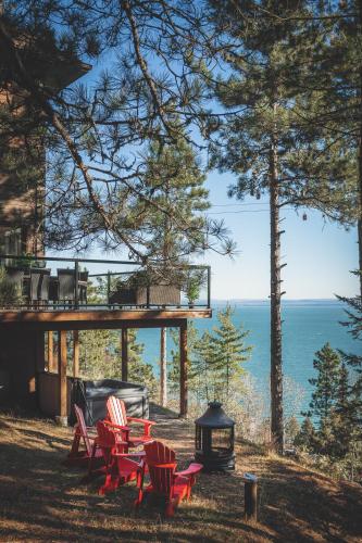 a group of red chairs and a grill with a view of the ocean at Villa Experience Nature Le Nid in Saint-Irénée