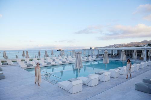 two women are standing next to a swimming pool at Mykonos Bay Resort & Villas in Mýkonos City