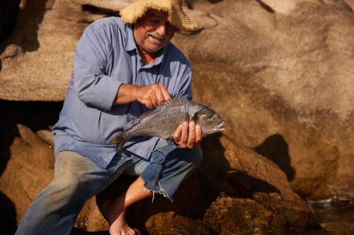 a man sitting on a rock holding a fish at Mykonos Bay Resort & Villas in Mýkonos City