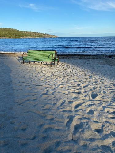 a green bench sitting on a beach near the water at Kleines Haus in Schweden in Viksjö