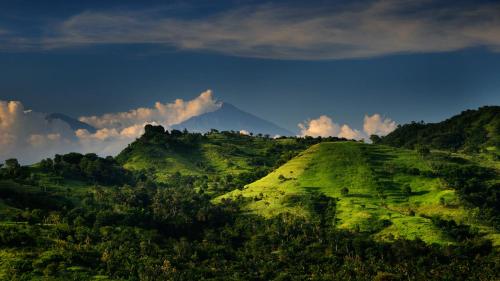 a green hill with a mountain in the background at DUNIA LOMBOK - Villas with Ocean View in Selong Belanak