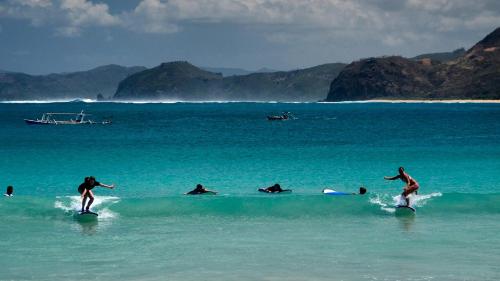 a group of people riding waves on surfboards in the ocean at DUNIA LOMBOK - Villas with Ocean View in Selong Belanak