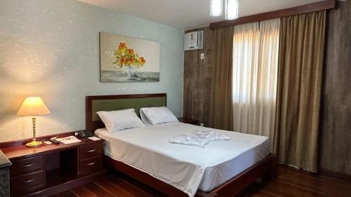 a bedroom with a bed and a table with a lamp at Hotel Du Lac Macaé in Macaé