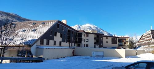 un bâtiment dans la neige avec une montagne en arrière-plan dans l'établissement LE BOIS DES COQS 1 Studio 2 à 3p Serre Chevalier 1350m avec balcon 5m2 parking et casier à ski, à Saint-Chaffrey