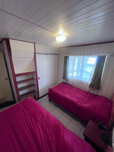 two beds in a small room with pink sheets at Cabañas Gabella in Lago Ranco