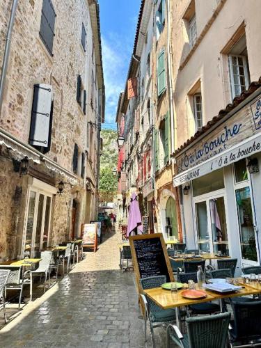 une femme qui marche dans une ruelle avec des tables et des chaises dans l'établissement Le Perchoir Du Parc Cœur historique Anduze 3 Etoiles, à Anduze