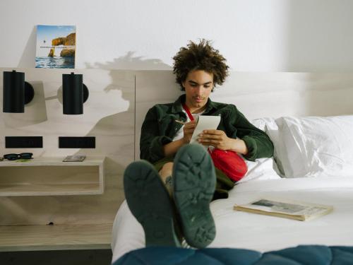 a woman sitting on a bed looking at a tablet at Field Station Joshua Tree in Yucca Valley