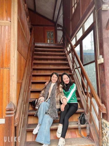two women sitting on the stairs of a cabin at Cầu Treo Homestay in Cham Ta Lao