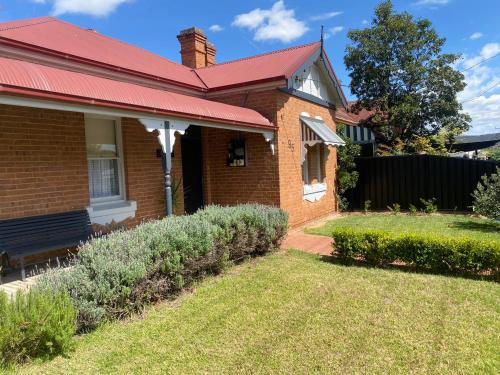 a brick house with a red roof and a yard at Merala a cosy cottage with easy stroll to CBD in Mudgee