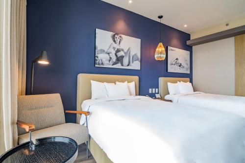 a hotel room with two beds and a chair at Torre Lucerna Hotel Ensenada in Ensenada