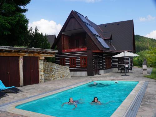 two people in a swimming pool in front of a house at Villa in Czechia with Heated Pool & Mountain Views in Vidochov