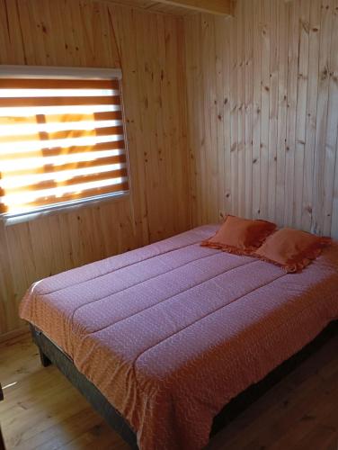 a bed in a wooden room with a window at Cabaña el descanso in Pelluhue