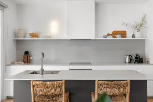 a white kitchen with a sink and two chairs at Drift at Palmstone - 2BR, Parking, Wifi in Glenelg