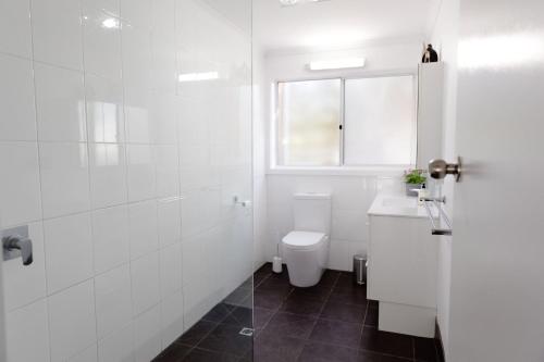 a white bathroom with a toilet and a window at Rockpool Cape Paterson in Cape Paterson